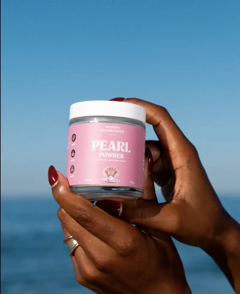Akasha Superfoods Pearl Powder jar held against a blue ocean sky
