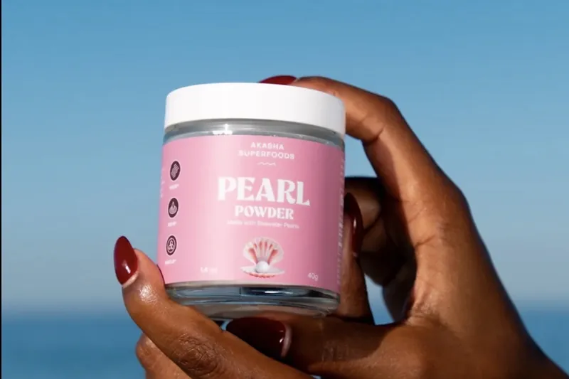 Akasha Superfoods Pearl Powder jar held up by the sea