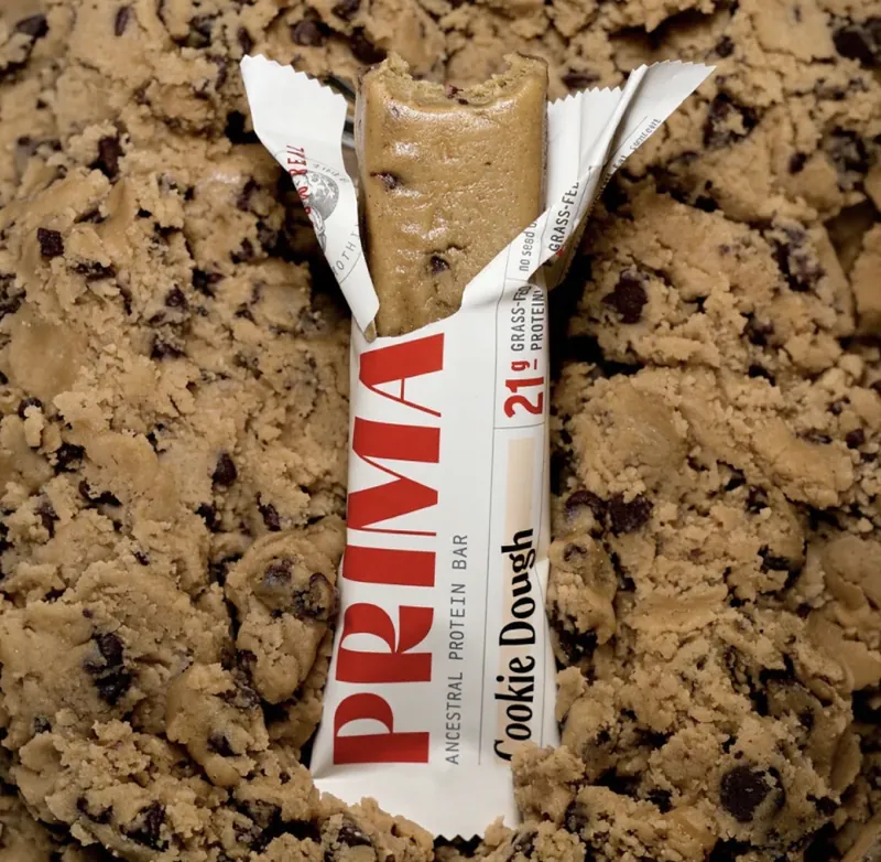 An opened Prima Cookie Dough protein bar in a bed of cookie dough