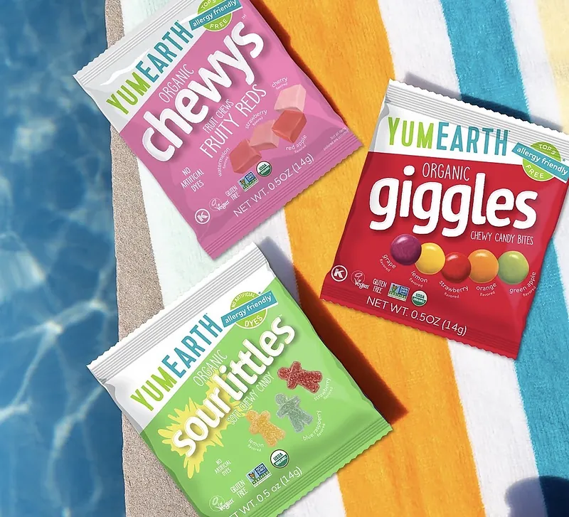 YumEarth organic Chewys, Giggles and Sour Littles packs on a striped towel by a pool